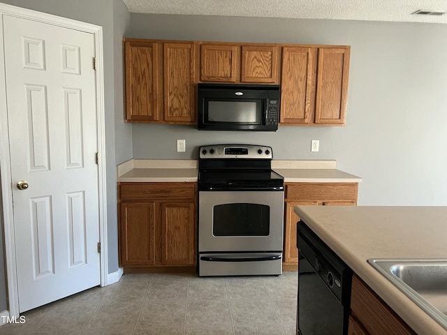 kitchen featuring light tile patterned floors, black appliances, sink, and a textured ceiling