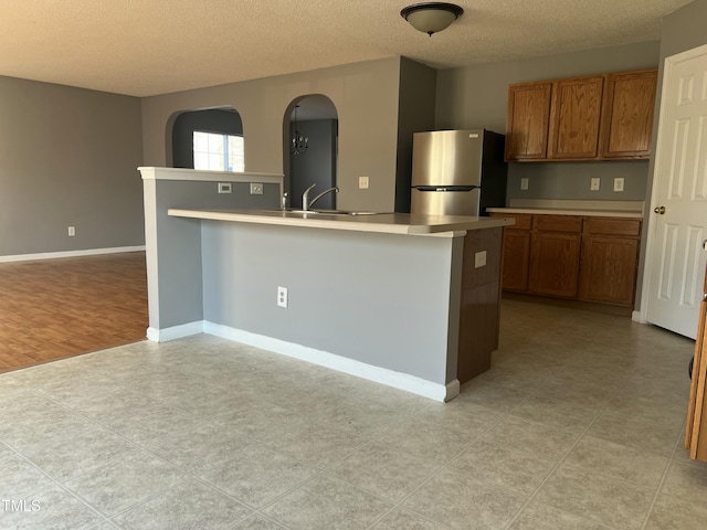 kitchen with a kitchen island with sink, sink, stainless steel refrigerator, and a textured ceiling