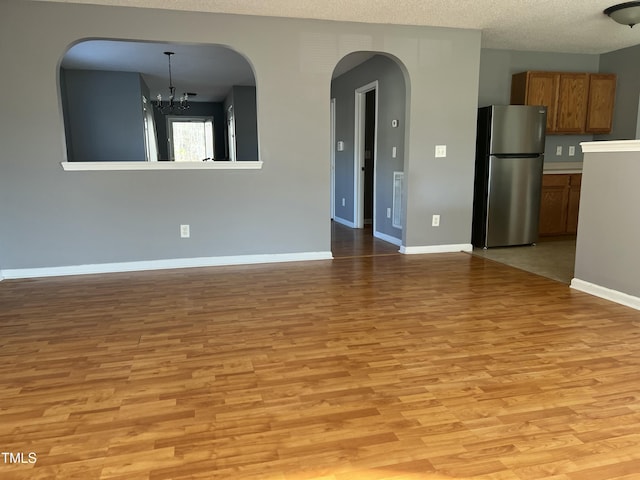 unfurnished living room featuring an inviting chandelier, a textured ceiling, and light wood-type flooring