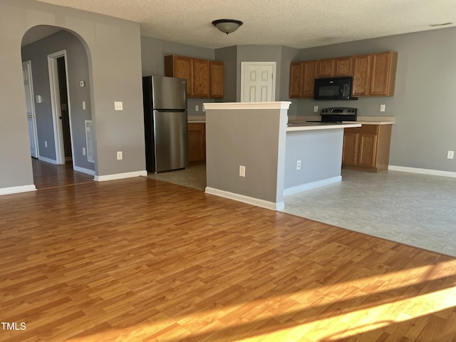 kitchen with stainless steel appliances, a center island, a textured ceiling, and light wood-type flooring