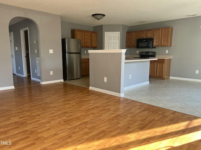 kitchen featuring light hardwood / wood-style flooring, stainless steel refrigerator, range with electric cooktop, a center island, and a textured ceiling