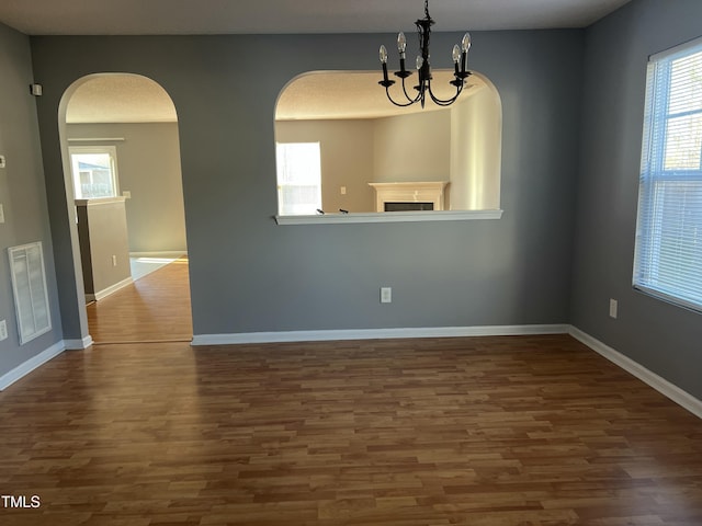 empty room with a notable chandelier and dark wood-type flooring