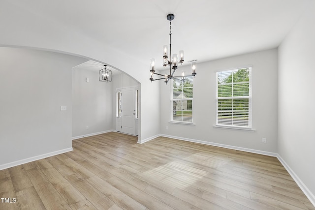 unfurnished dining area with light wood finished floors, arched walkways, a notable chandelier, and baseboards