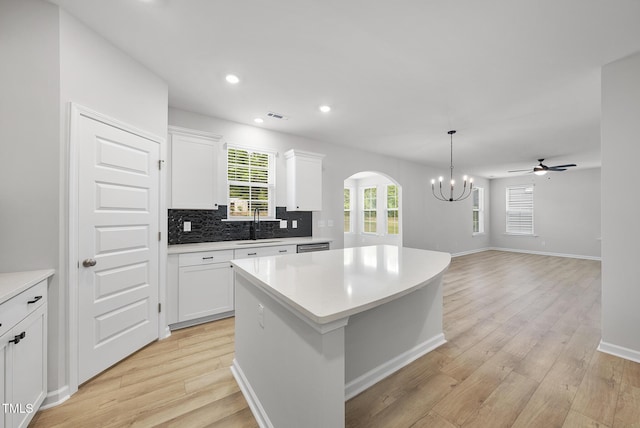 kitchen with white cabinets, light wood-style flooring, light countertops, arched walkways, and a center island
