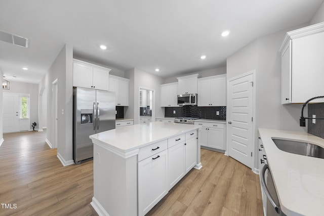 kitchen with appliances with stainless steel finishes, backsplash, a center island, a sink, and light wood-type flooring