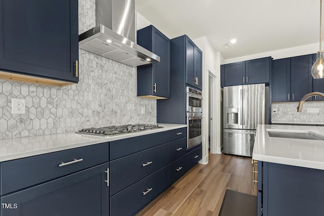 kitchen with blue cabinets, appliances with stainless steel finishes, sink, and wall chimney exhaust hood