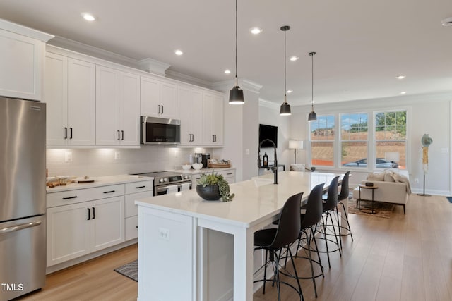 kitchen featuring appliances with stainless steel finishes, a breakfast bar, decorative light fixtures, white cabinetry, and an island with sink