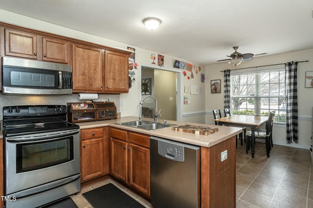 kitchen with appliances with stainless steel finishes, sink, backsplash, ceiling fan, and kitchen peninsula