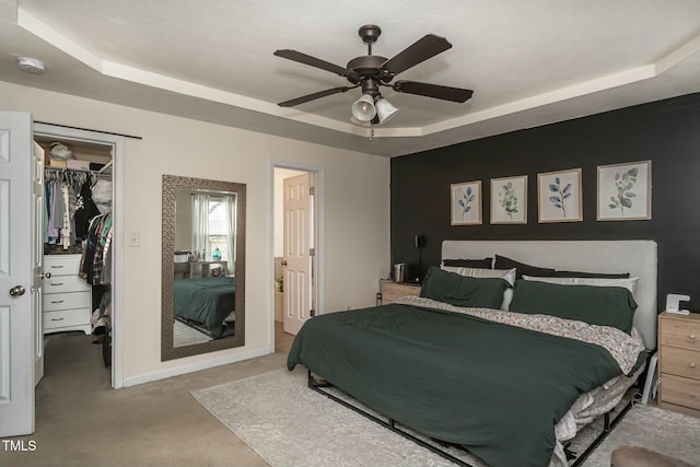 carpeted bedroom with ensuite bath, a spacious closet, a tray ceiling, a closet, and ceiling fan