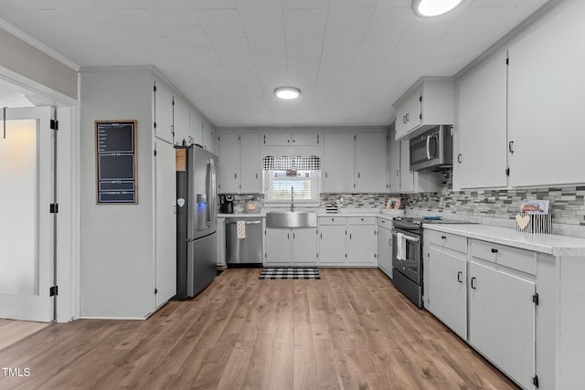 kitchen featuring sink, tasteful backsplash, ornamental molding, appliances with stainless steel finishes, and light hardwood / wood-style floors