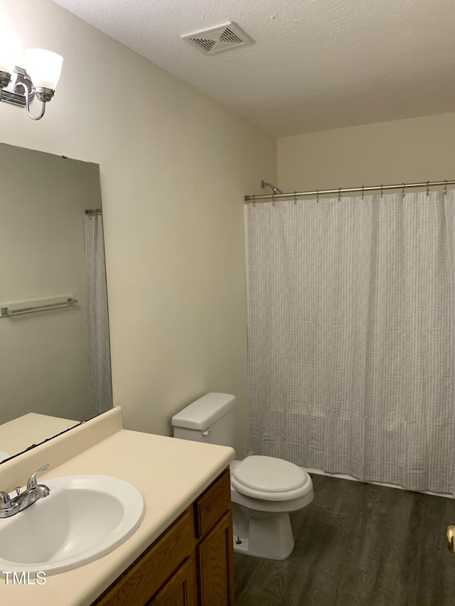 bathroom featuring visible vents, toilet, a textured ceiling, vanity, and wood finished floors