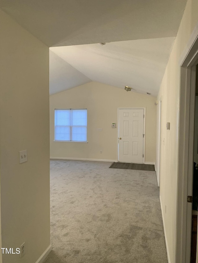 carpeted spare room featuring lofted ceiling and baseboards