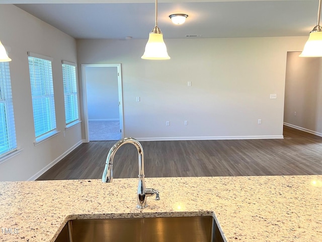 kitchen featuring light stone counters, dark wood-type flooring, sink, and hanging light fixtures