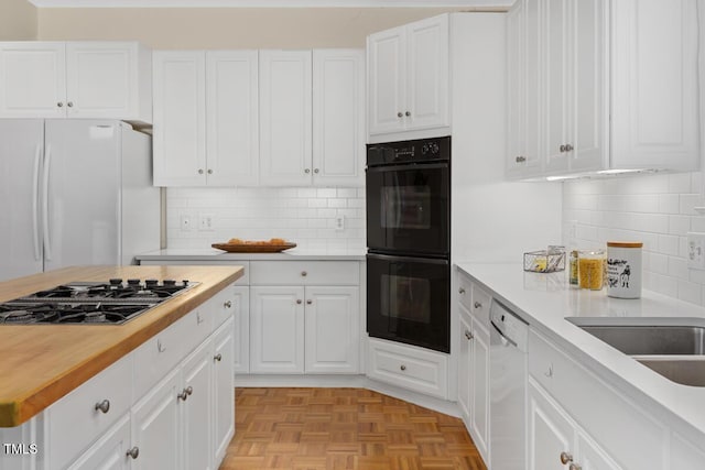 kitchen with white appliances, light parquet flooring, butcher block counters, and white cabinets