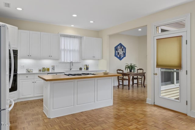 kitchen with butcher block countertops, gas stovetop, white cabinetry, a kitchen island, and light parquet flooring