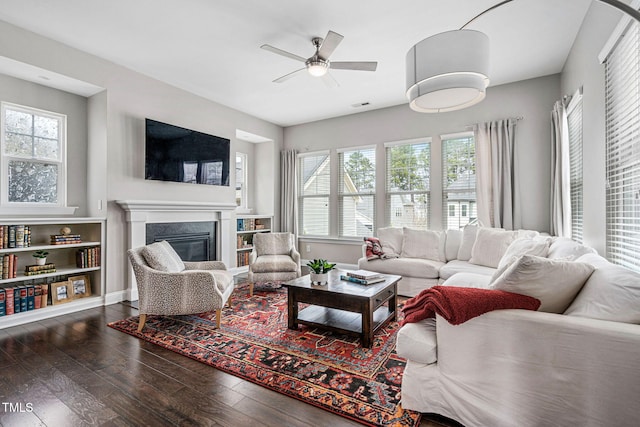 living room featuring a premium fireplace, visible vents, ceiling fan, and wood-type flooring