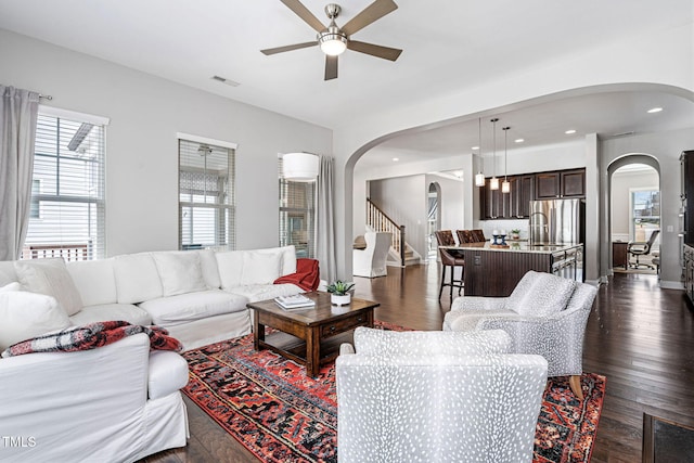 living area with visible vents, ceiling fan, dark wood finished floors, stairs, and arched walkways