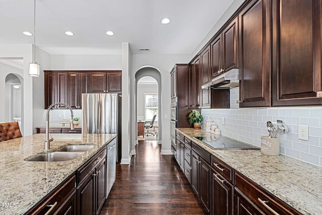 kitchen featuring light stone countertops, dark wood-style flooring, arched walkways, stainless steel appliances, and under cabinet range hood