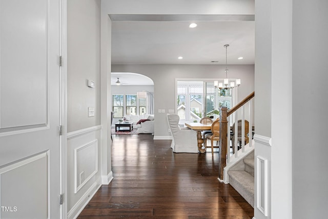 hallway with a notable chandelier, dark wood-type flooring, recessed lighting, arched walkways, and stairs