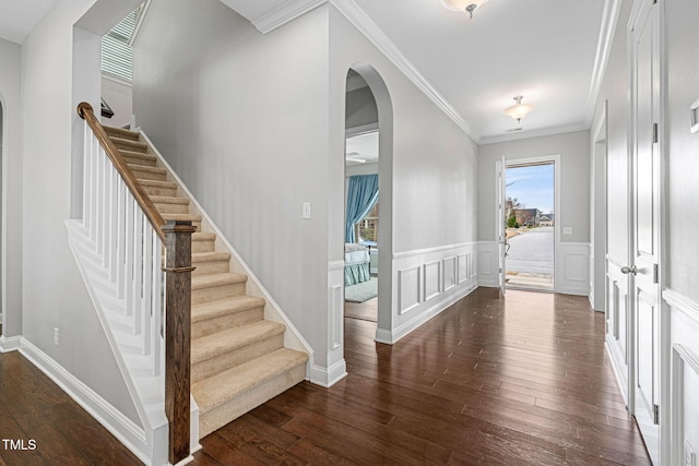 foyer entrance featuring arched walkways, dark wood finished floors, wainscoting, and ornamental molding