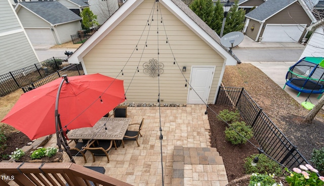 rear view of house with a detached garage, a trampoline, a fenced backyard, and a patio area