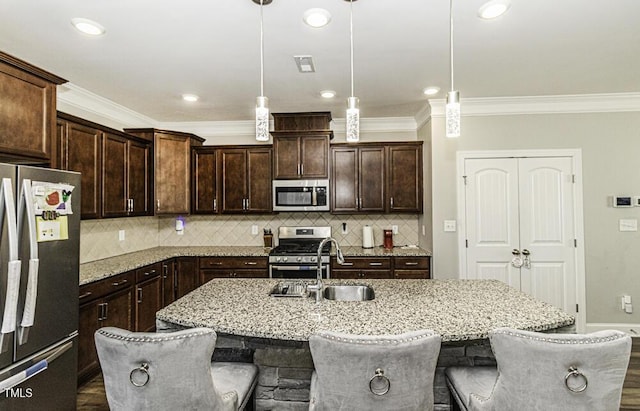 kitchen featuring a kitchen bar, hanging light fixtures, a center island with sink, and appliances with stainless steel finishes