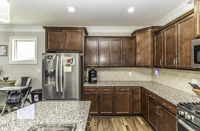 kitchen featuring light stone countertops, appliances with stainless steel finishes, ornamental molding, and dark brown cabinets