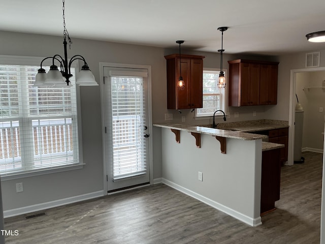 kitchen with decorative light fixtures, sink, a kitchen bar, kitchen peninsula, and dark wood-type flooring