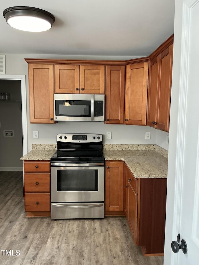 kitchen with light stone countertops, stainless steel appliances, and light hardwood / wood-style floors