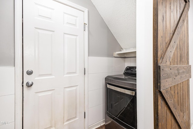 laundry area featuring a barn door, washer / dryer, tile walls, and a textured ceiling