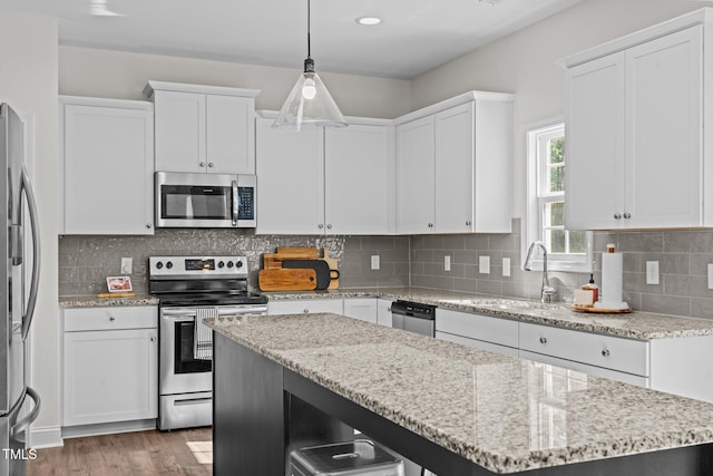 kitchen featuring tasteful backsplash, hanging light fixtures, white cabinets, and appliances with stainless steel finishes