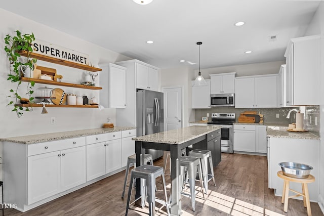 kitchen featuring appliances with stainless steel finishes, a kitchen island, white cabinets, a kitchen bar, and decorative light fixtures