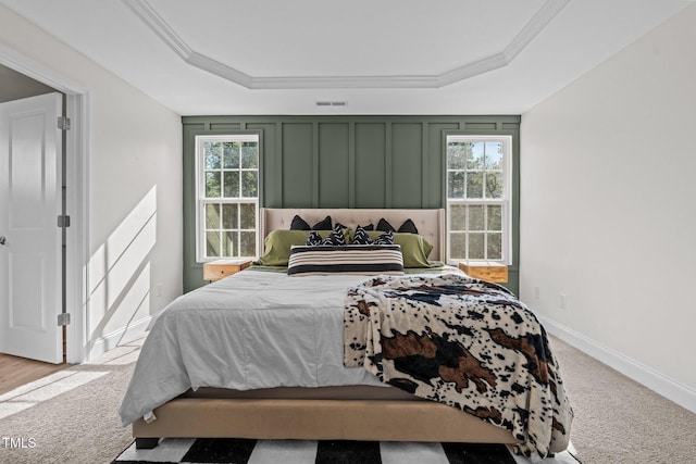 carpeted bedroom featuring ornamental molding, a raised ceiling, and multiple windows