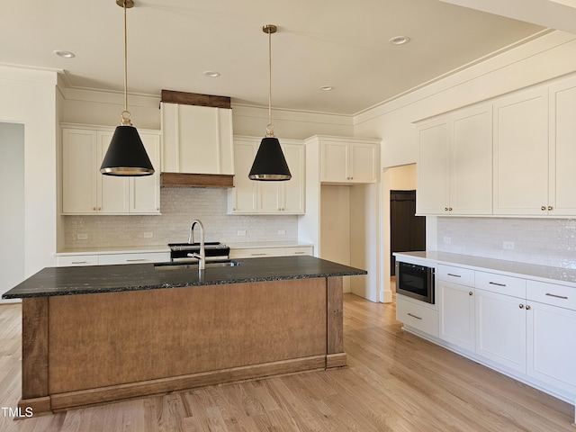 kitchen with built in microwave, white cabinetry, pendant lighting, and a center island with sink