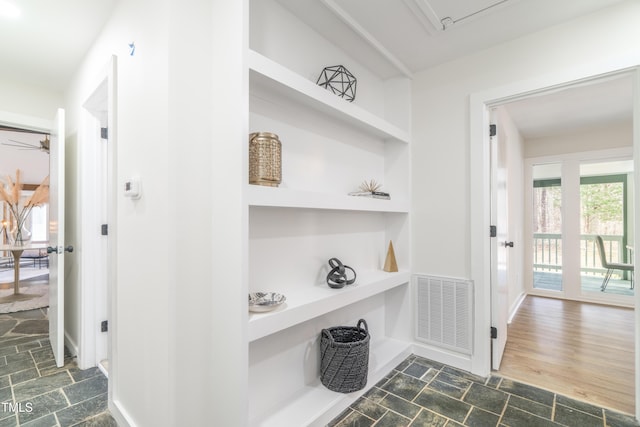 hallway with stone tile floors, built in shelves, visible vents, and baseboards