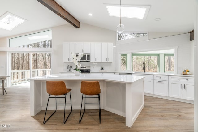 kitchen featuring vaulted ceiling with skylight, white cabinets, a center island, stainless steel appliances, and a sink