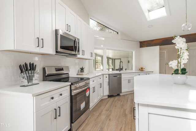 kitchen with white cabinets, vaulted ceiling with skylight, stainless steel appliances, and decorative backsplash