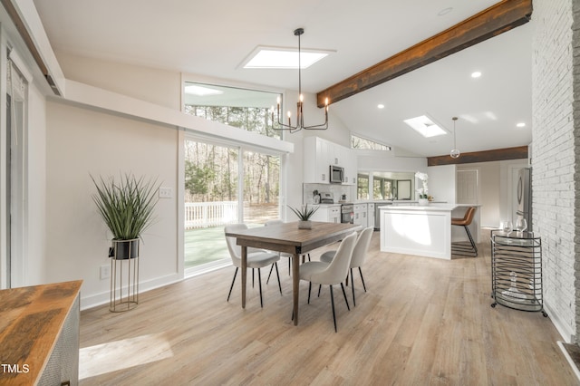 dining space with light wood finished floors, a skylight, beamed ceiling, an inviting chandelier, and high vaulted ceiling