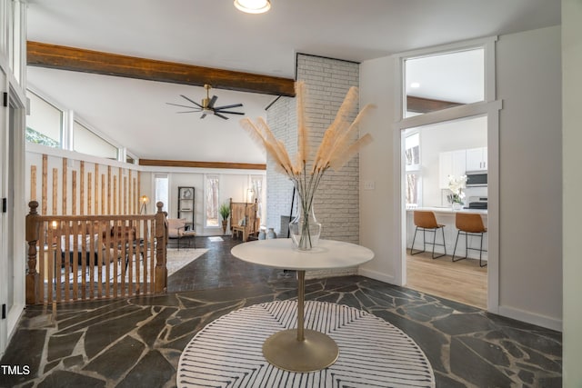 interior space with a ceiling fan, vaulted ceiling with beams, and baseboards