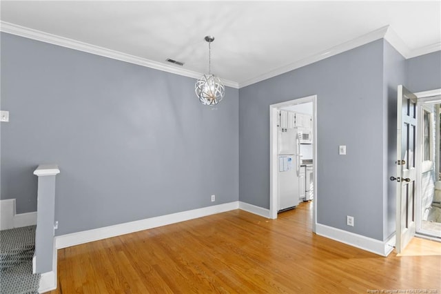 spare room featuring wood-type flooring, ornamental molding, and a chandelier