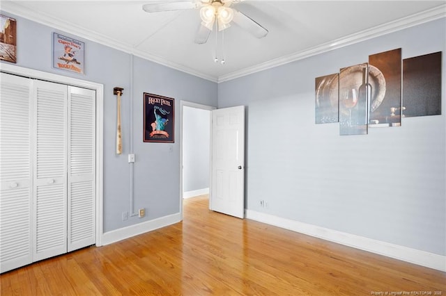 unfurnished bedroom with ornamental molding, wood-type flooring, ceiling fan, and a closet