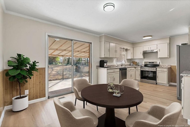 dining space with light wood-type flooring, wainscoting, wooden walls, and crown molding