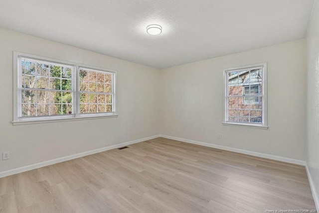 spare room featuring light wood finished floors, visible vents, and baseboards