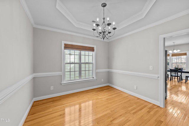 empty room with a chandelier, light wood-type flooring, a raised ceiling, and baseboards