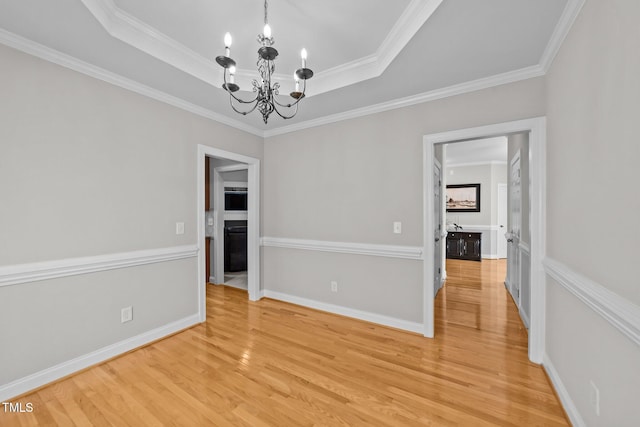 unfurnished room with baseboards, a raised ceiling, light wood-style flooring, ornamental molding, and an inviting chandelier