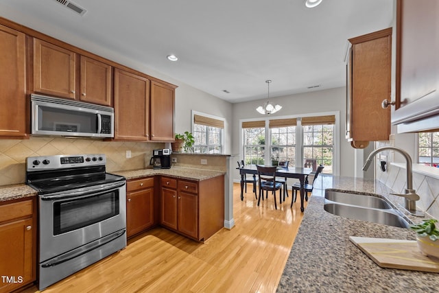 kitchen featuring brown cabinets, a peninsula, stainless steel appliances, and a sink