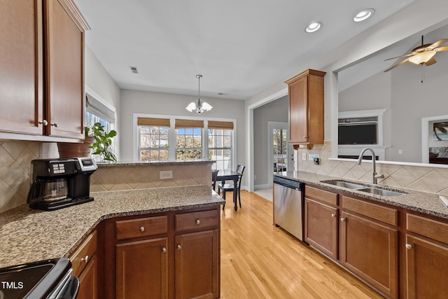 kitchen featuring stainless steel appliances, a sink, light stone countertops, light wood-type flooring, and a peninsula