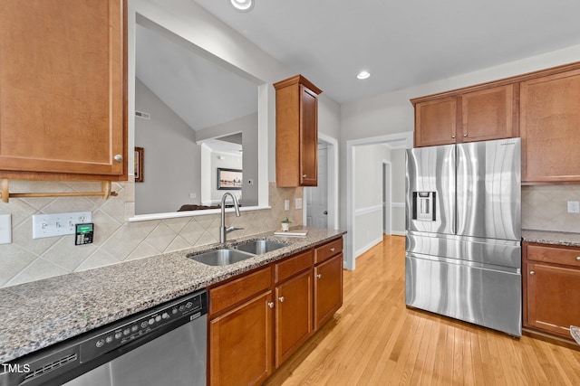 kitchen featuring light stone countertops, a sink, appliances with stainless steel finishes, brown cabinets, and light wood finished floors