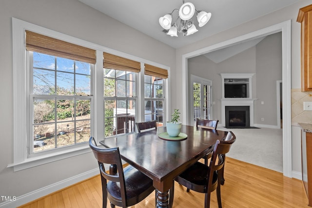 dining room featuring baseboards, a fireplace with flush hearth, vaulted ceiling, light wood-type flooring, and a notable chandelier