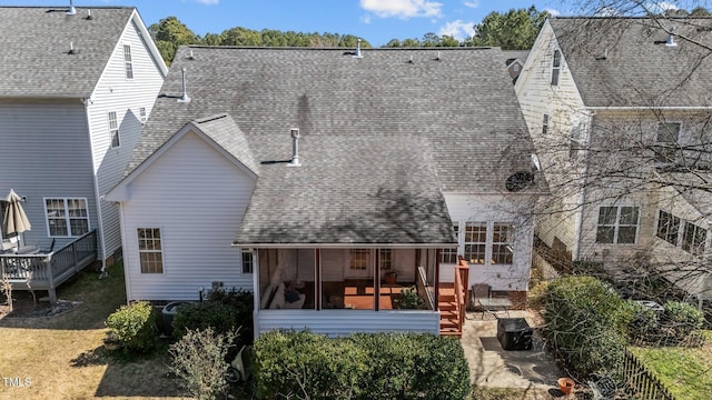 rear view of property featuring a deck, a patio, a shingled roof, a sunroom, and a yard